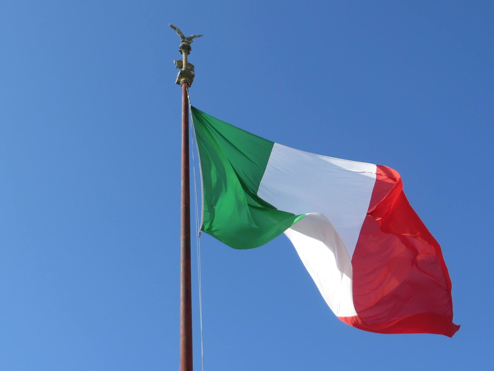 close up of the italian flag on a flagpole against a clear blue sky